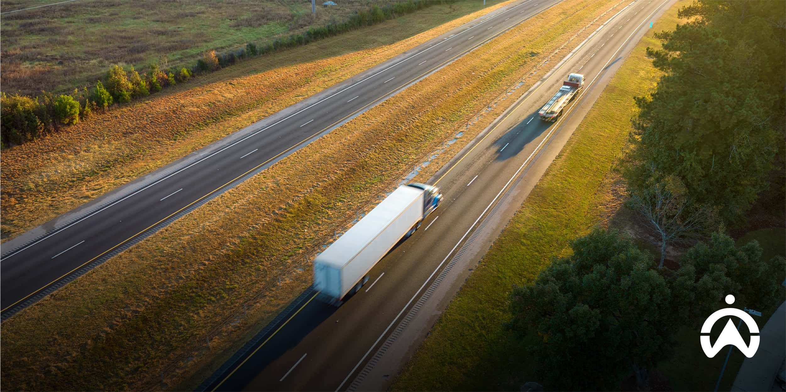 Two commercial fleet trucks driving on a highway during golden hour for fleet compliance.